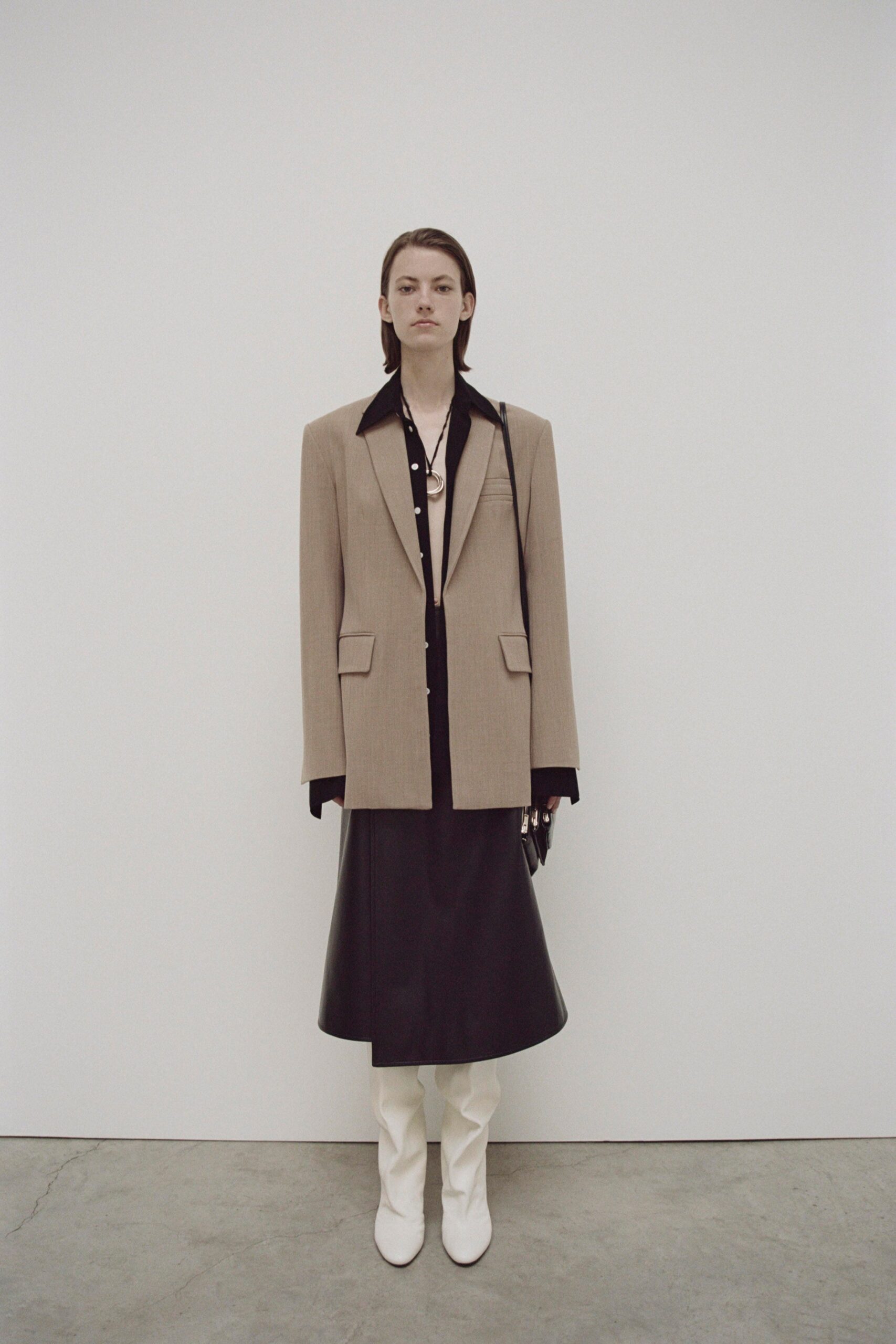A fitted beige blazer paired with a black leather skirt, featuring long sleeves and a collared design.