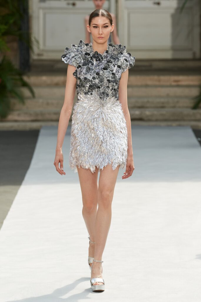 A fitted silver silk sleeveless dress with a high neckline and ruffled tiered design.