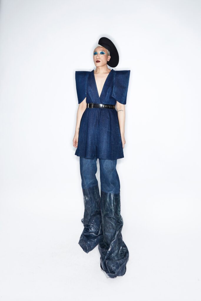 A fitted blue denim sleeveless dress with a V-neckline and asymmetric design paired with unique pants.