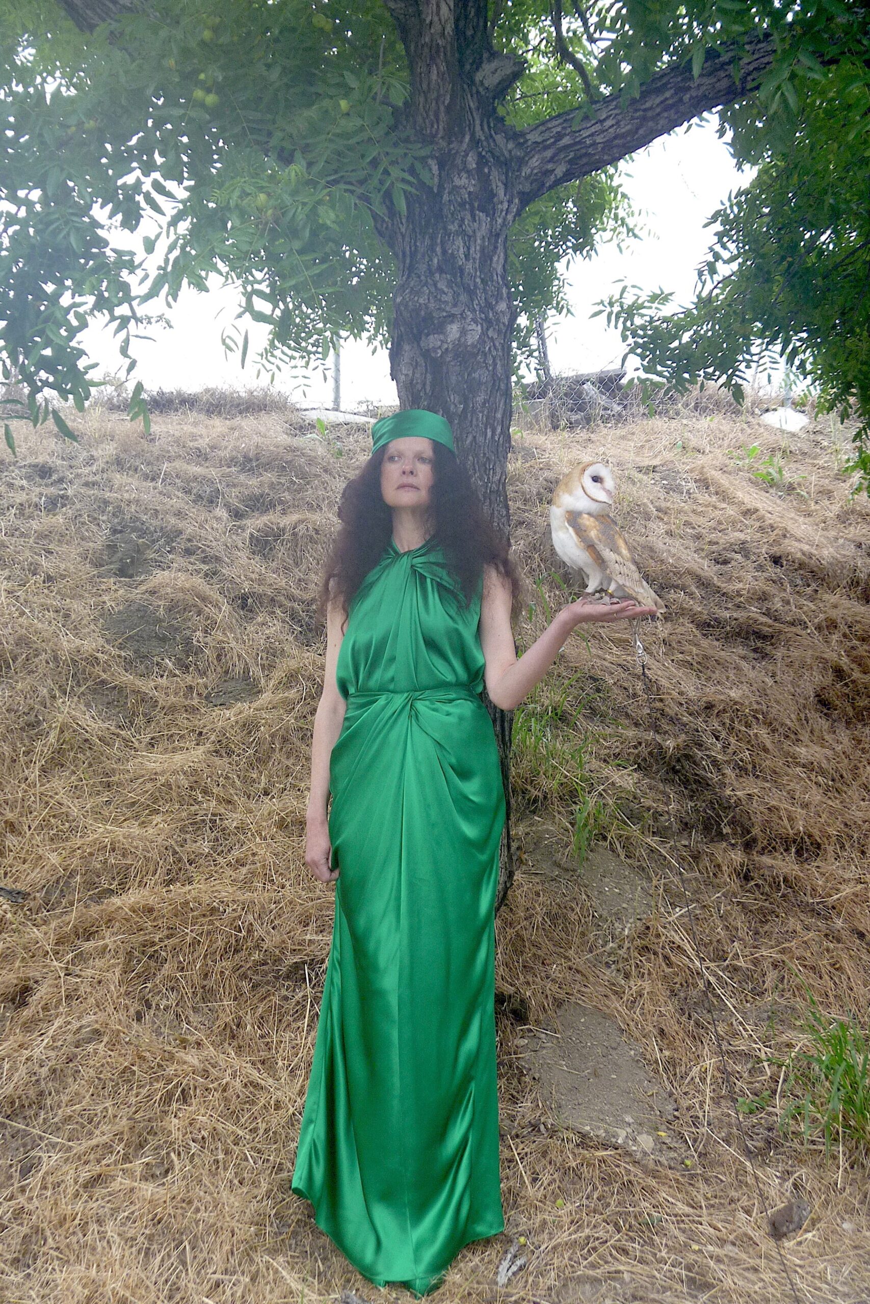 A fitted green silk sleeveless dress with a high neckline and draped design.