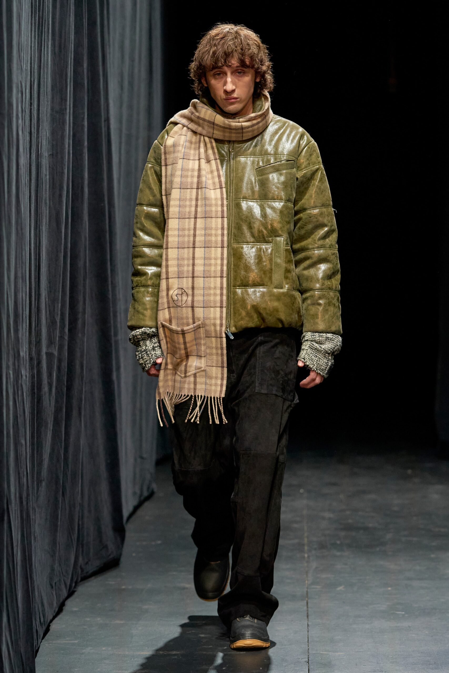 A relaxed green leather jacket paired with black pants, featuring a zippered design detail.