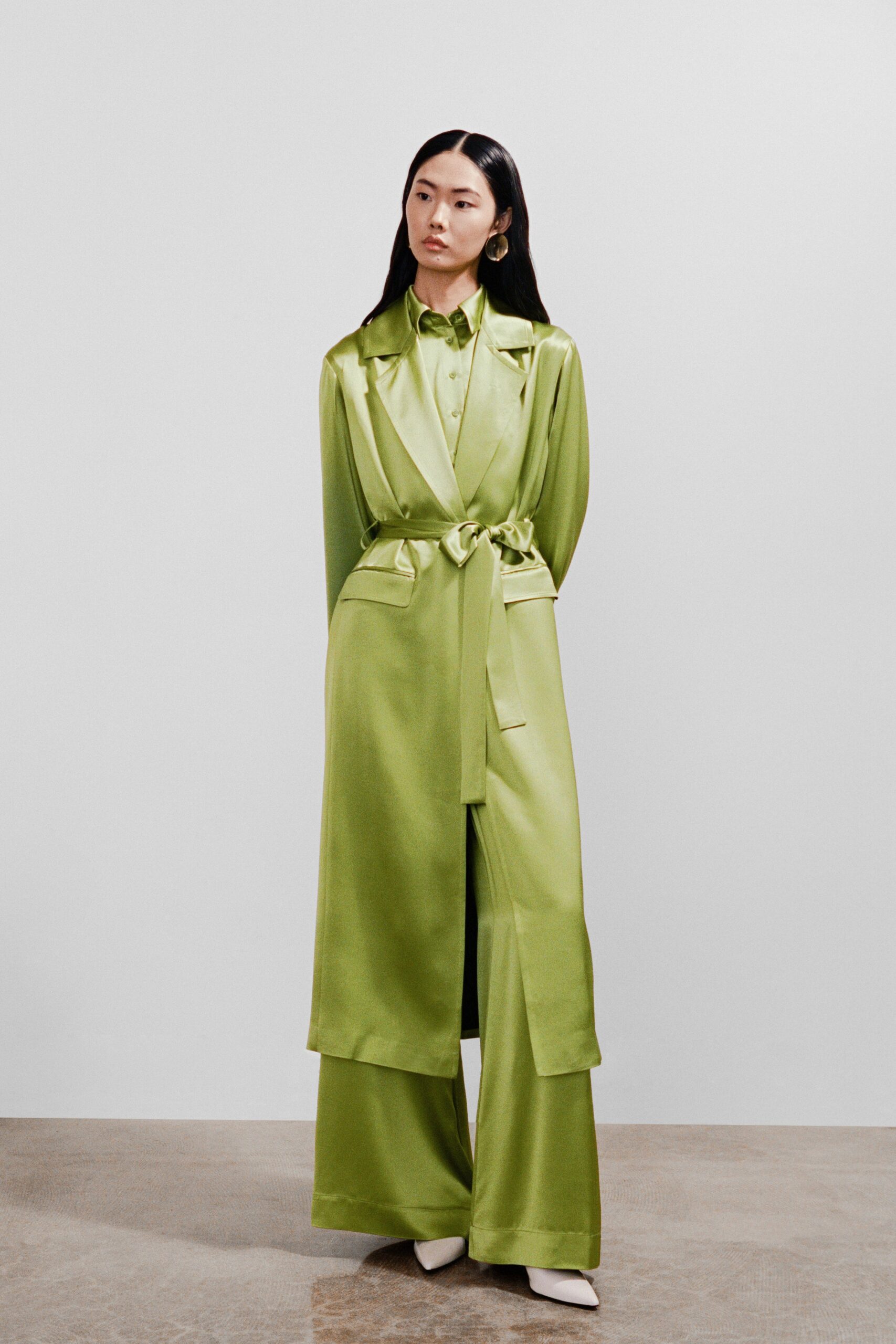 A relaxed green silk coat with a belted waist paired with wide-leg pants.