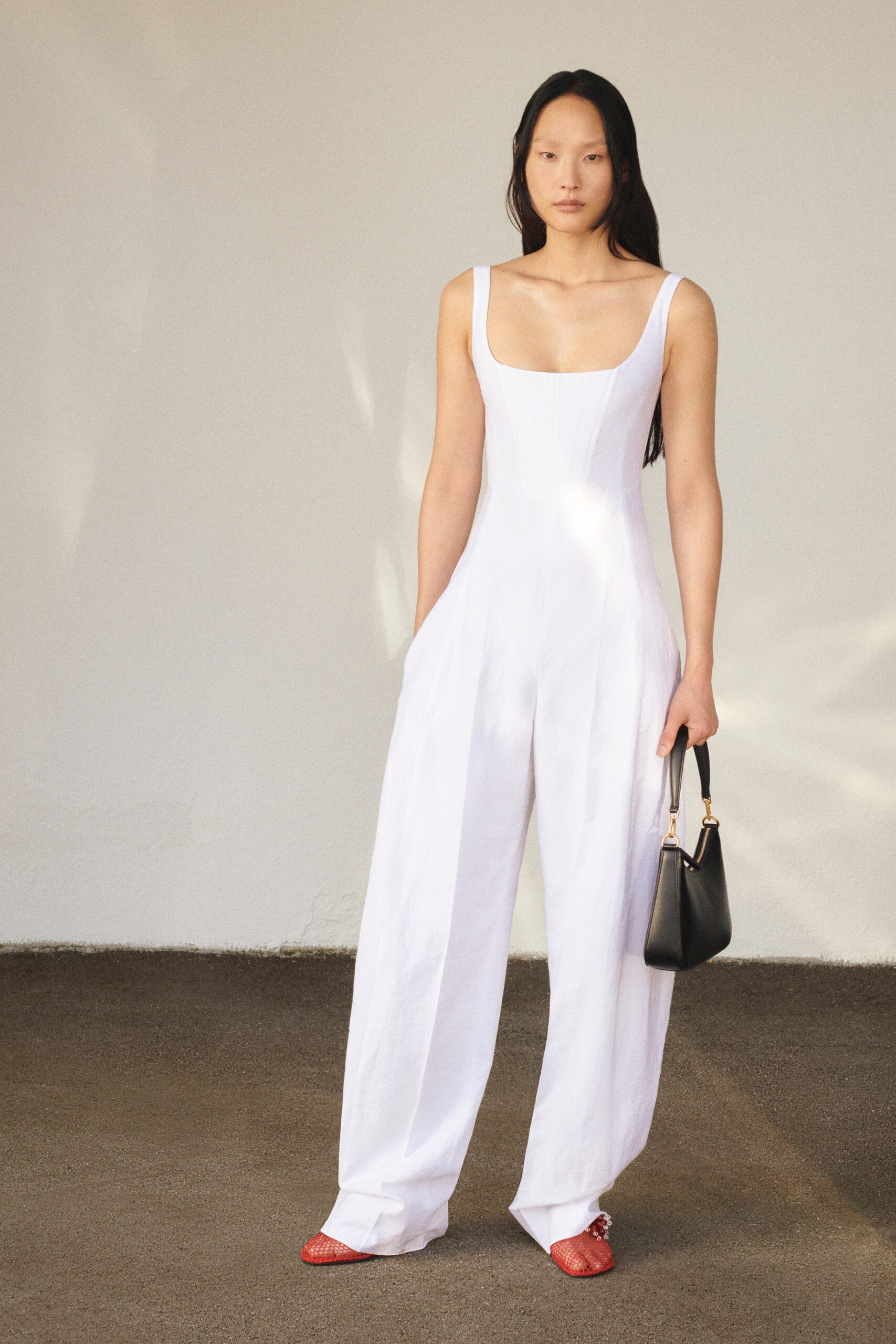 A relaxed white cotton sleeveless jumpsuit featuring a square neckline and pleated details.