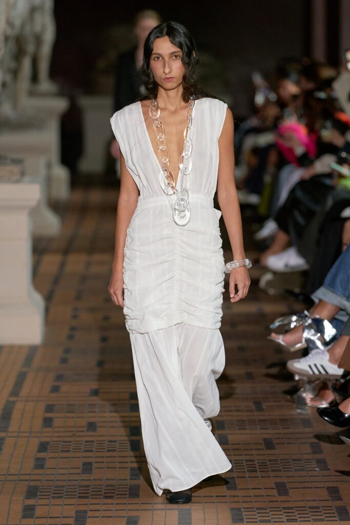 A fitted white silk sleeveless dress with a V-neckline and pleated design.