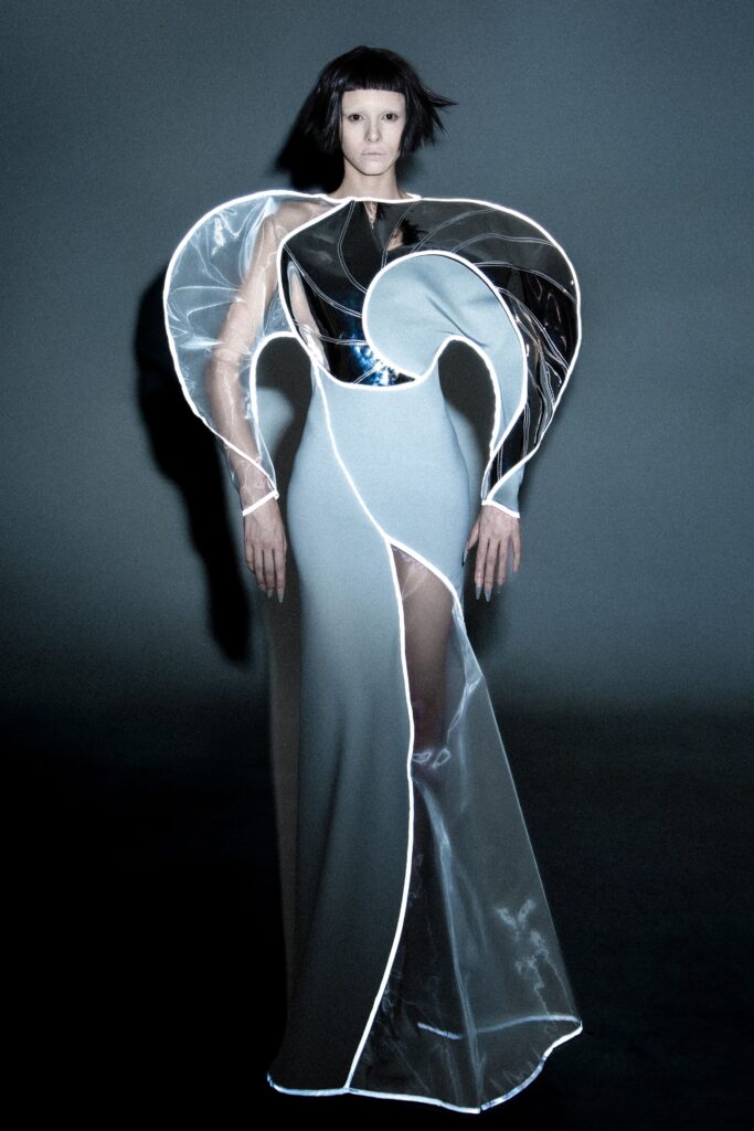 A fitted black and gray dress with long sleeves, high neckline, and an asymmetric draped design.