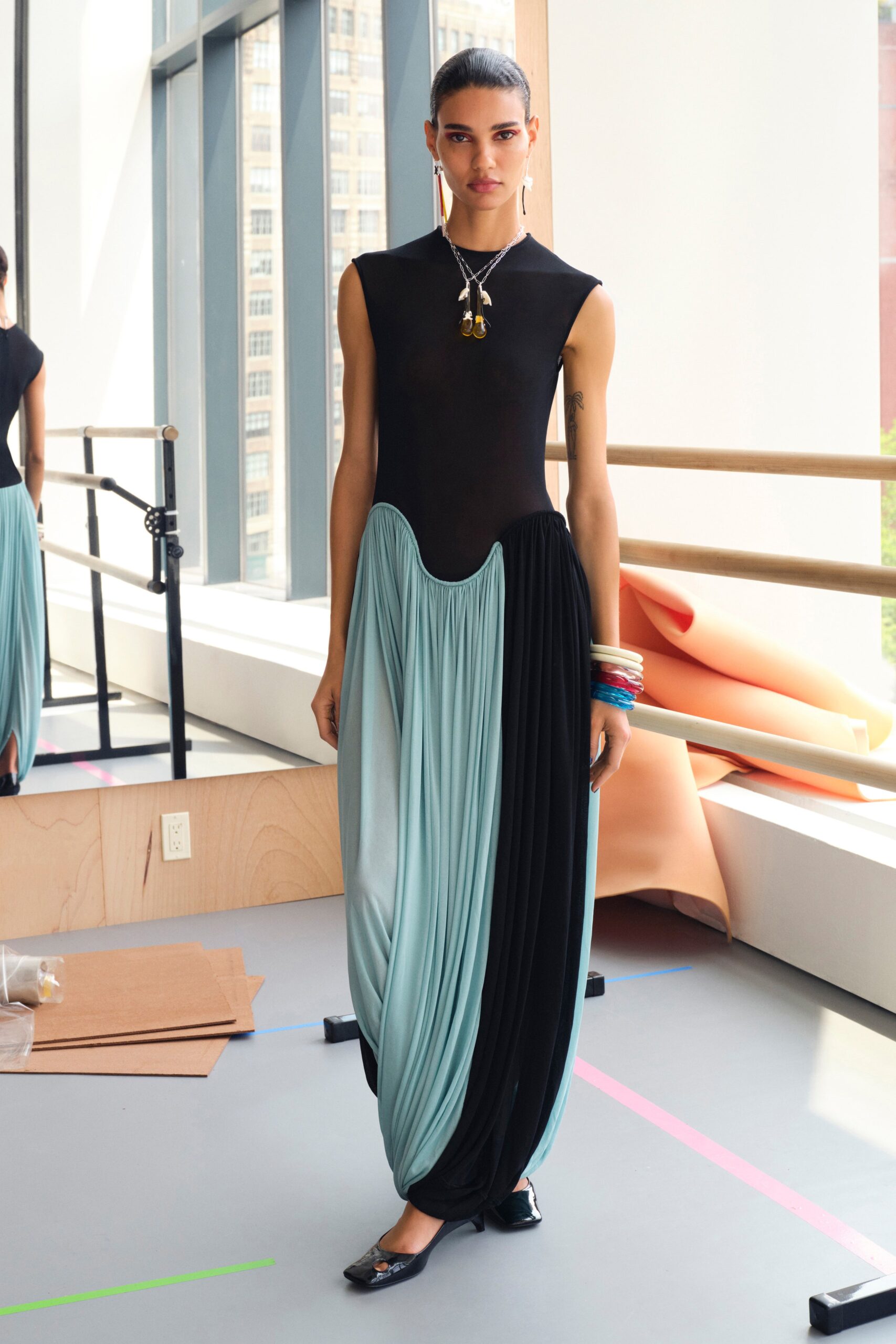A fitted sleeveless dress featuring a high-neck and asymmetric pleated design in black and blue.