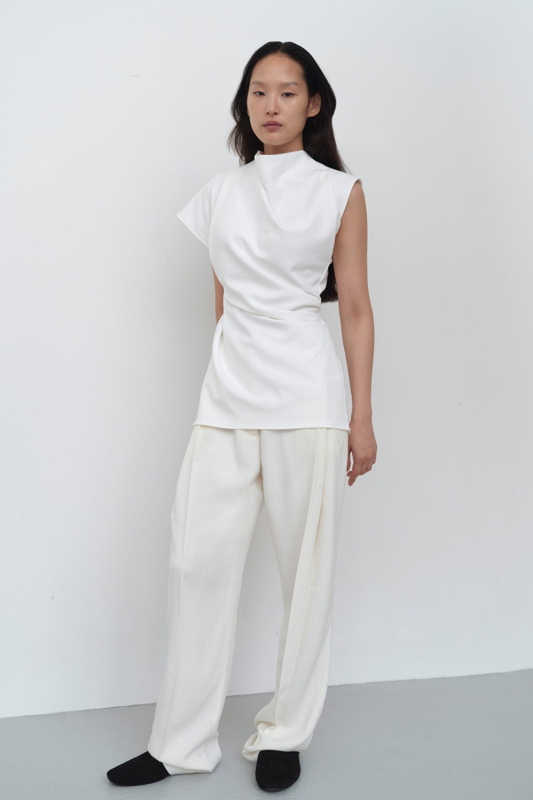 A relaxed white sleeveless top with a high-neck and asymmetric design paired with matching pants.