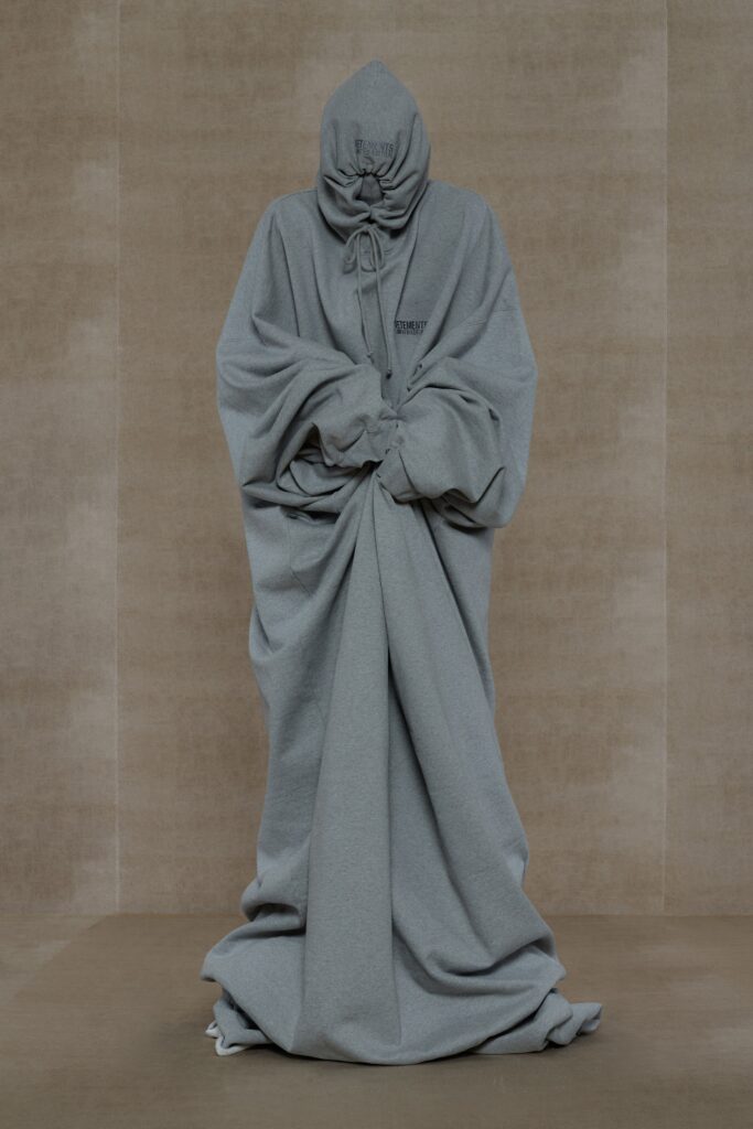 An oversized gray cotton coat with a hood and draped design.