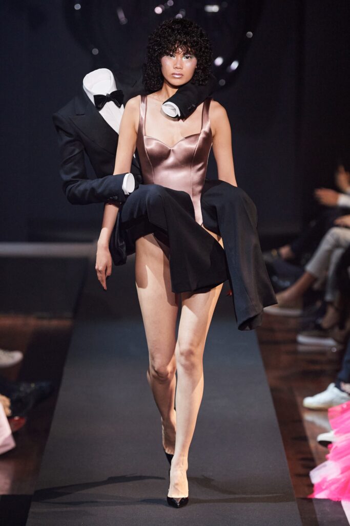 A fitted pink silk bodysuit paired with a structured black jacket, showcasing a modern runway look.