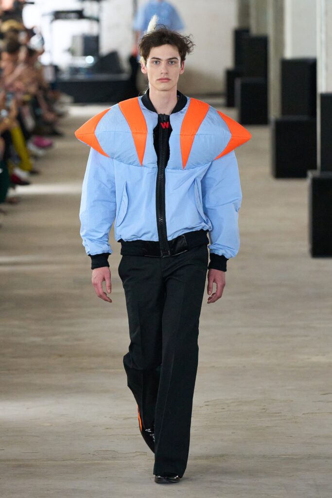 A relaxed-fit blue jacket with orange accents paired with black pants.
