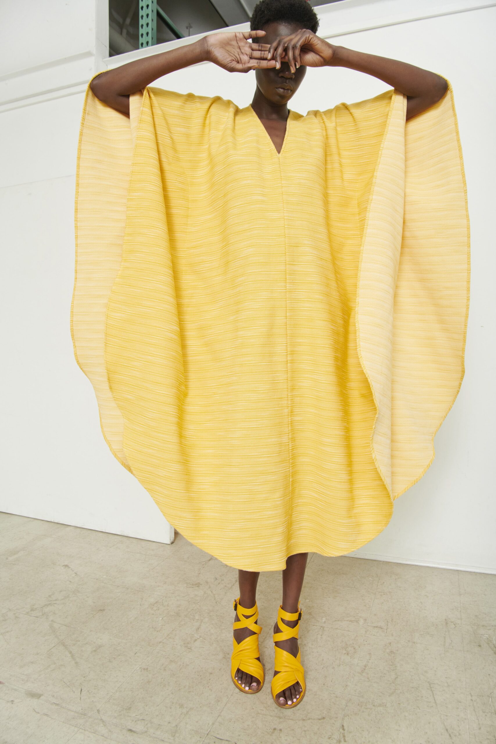 A relaxed yellow sleeveless dress with a V-neckline and asymmetric silhouette.