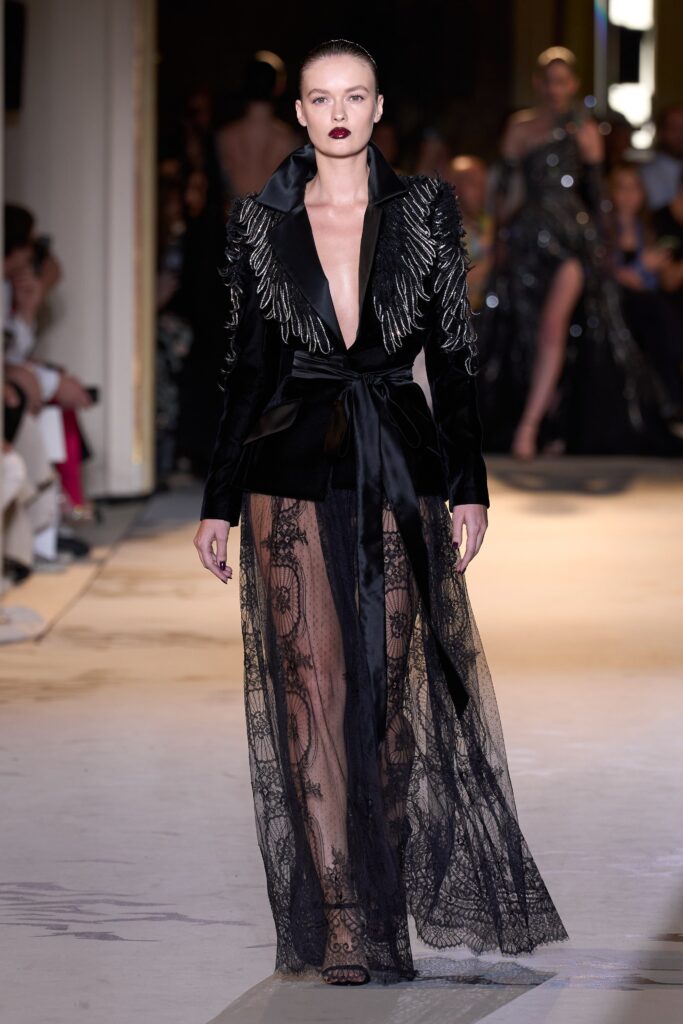 A fitted black silk dress with long sleeves, a V-neckline, and sheer embroidered details.