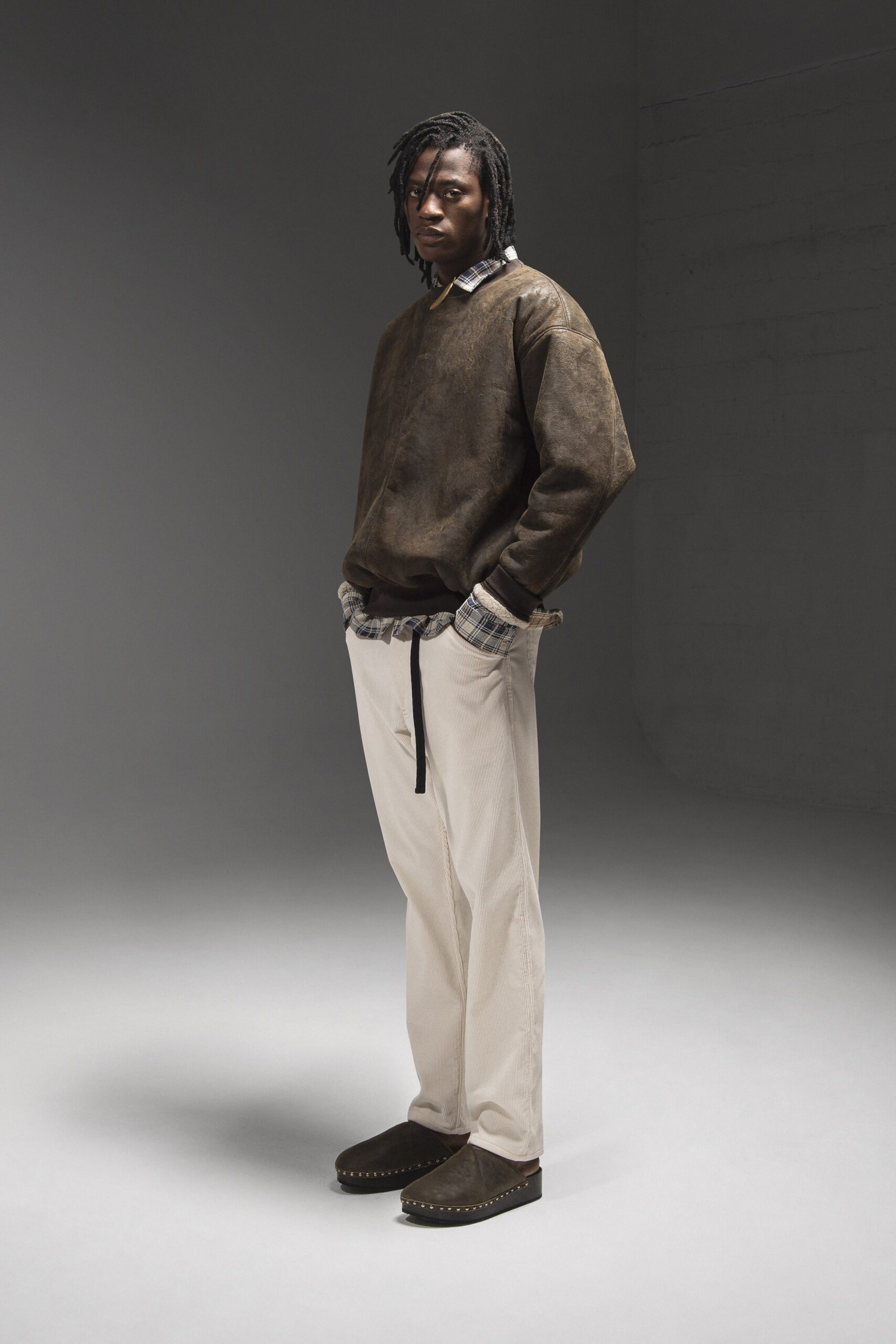 A relaxed brown leather long-sleeve sweater paired with beige striped pants.