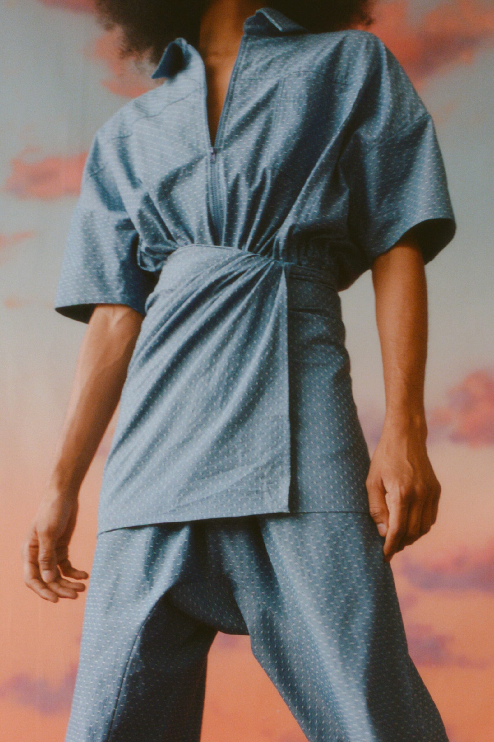 This relaxed ensemble features a short-sleeve top with a distinctive collar, elegantly cinched at the waist to create an asymmetric silhouette. The flowing pants complement the top's structure, resulting in a harmonious blend of movement and style.