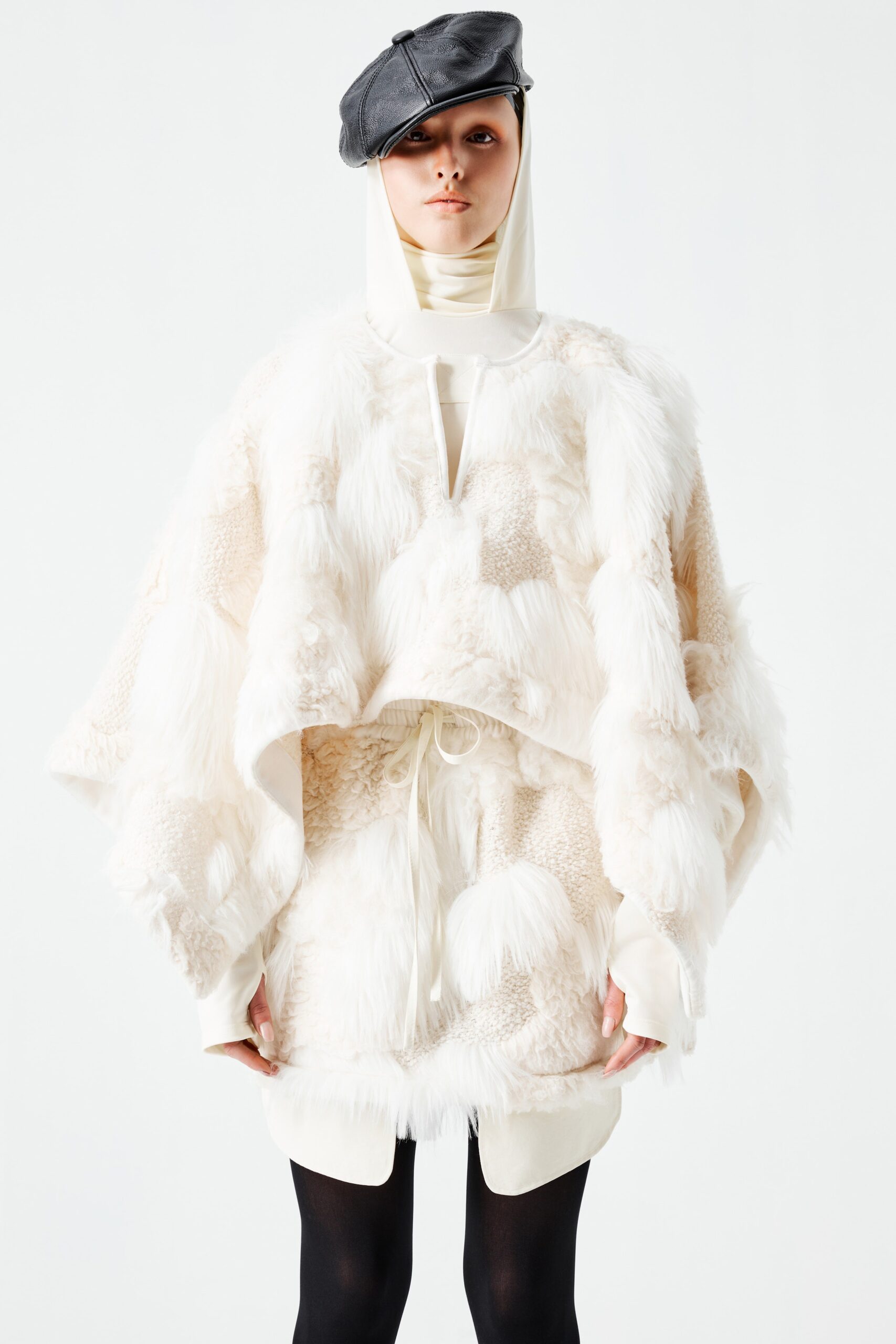 This oversized poncho dress in white fur showcases a unique layered texture that adds depth and dimension. The high-neck construction enhances its sculptural silhouette, creating a striking visual impact that redefines contemporary outerwear.