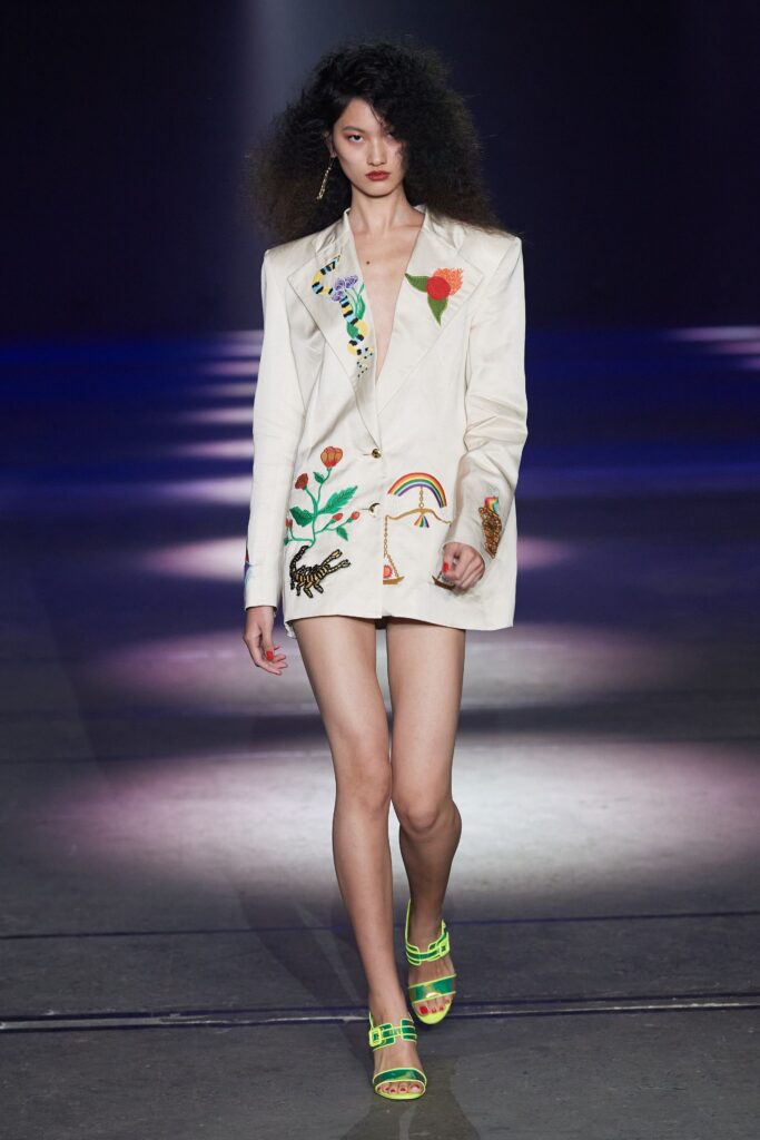 A fitted white blazer dress with long sleeves, V-neckline, and embroidered details.