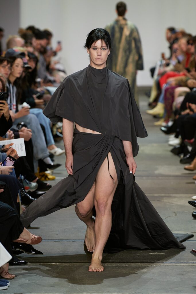 A relaxed black sleeveless dress with a high neckline and asymmetric design featuring a slit.