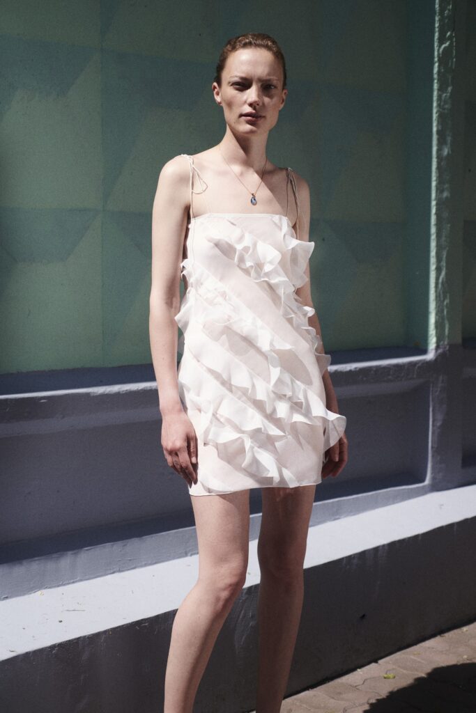 A fitted white silk sleeveless dress featuring a V-neckline and ruffled detailing.