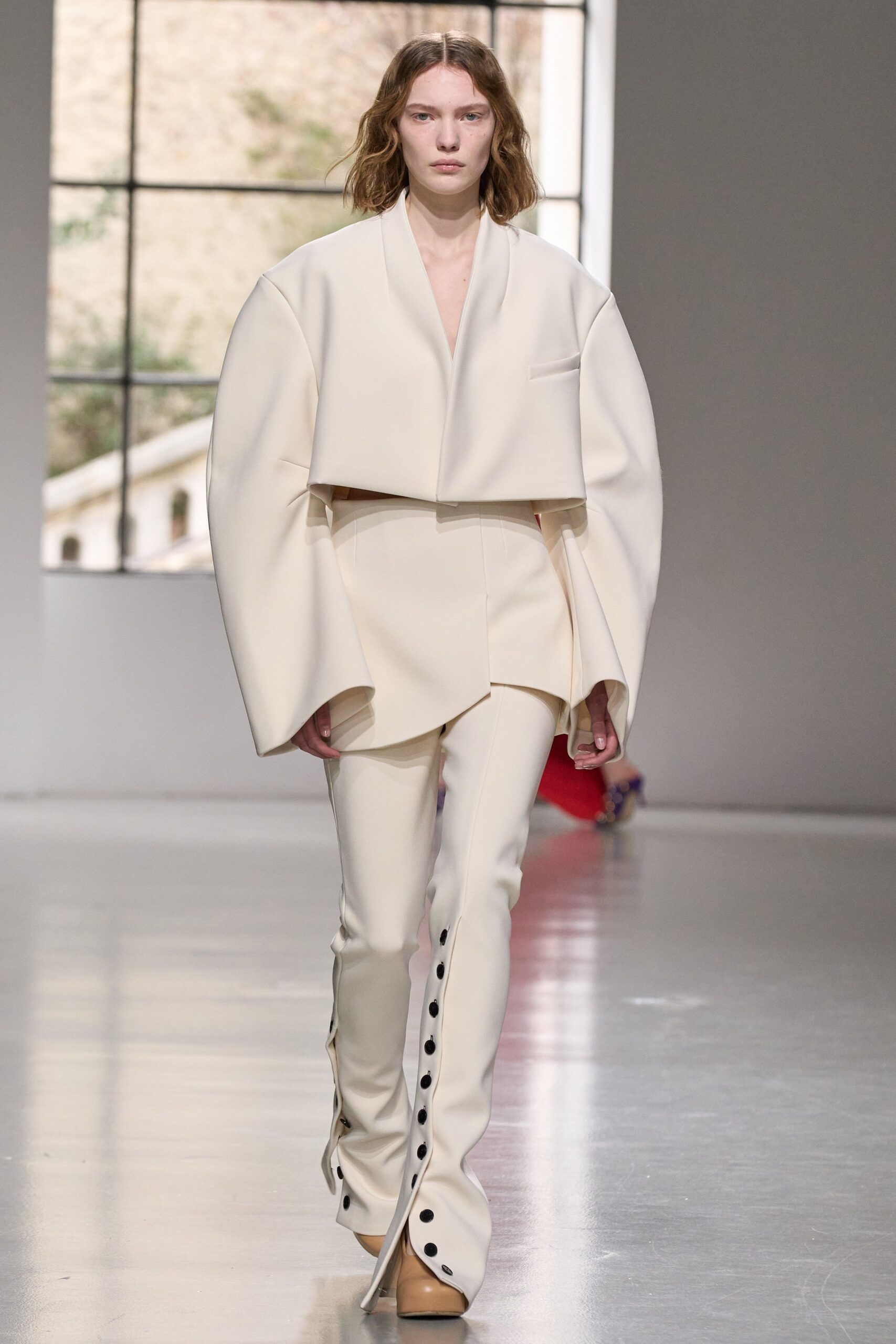 A relaxed white jacket with long sleeves and asymmetric design paired with buttoned pants.