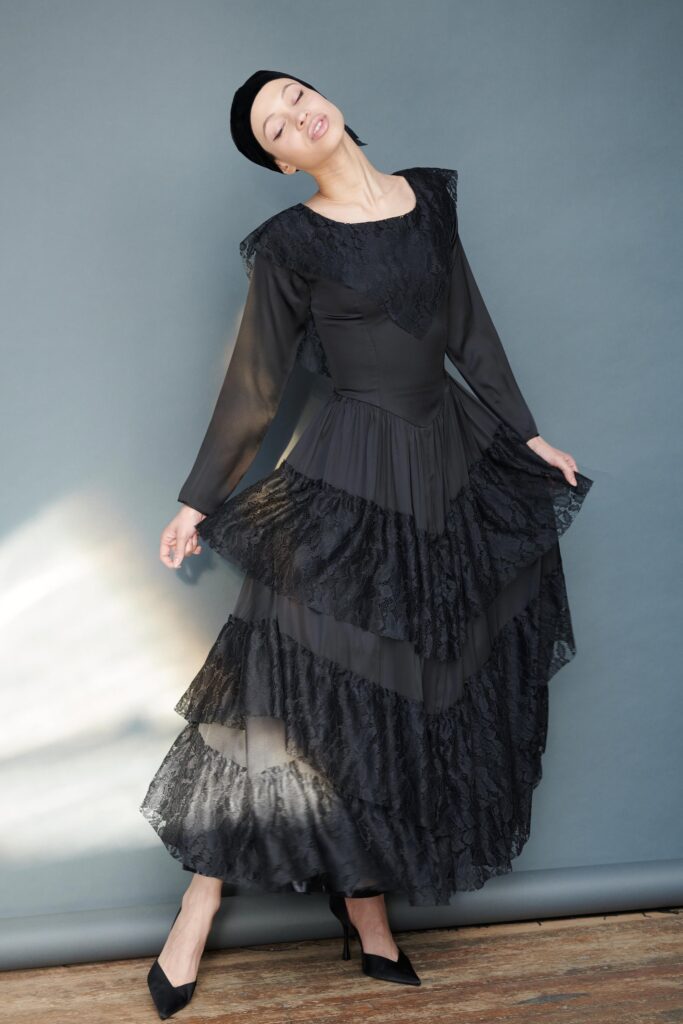 A fitted black lace long-sleeve dress with a high neckline and tiered design.