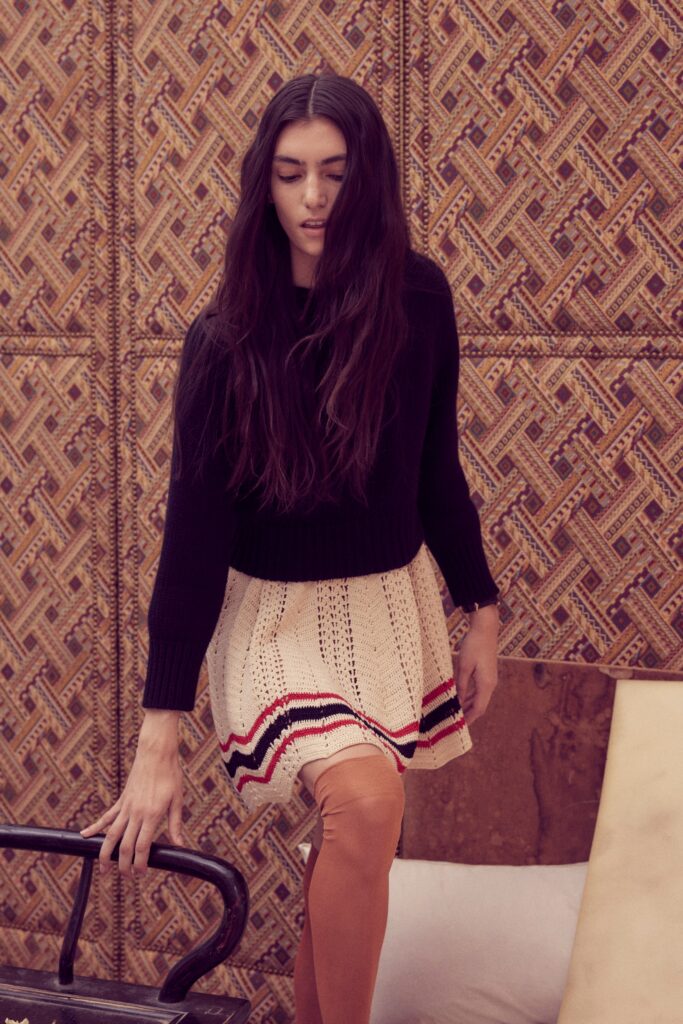 A fitted black long-sleeve sweater paired with a cream pleated skirt featuring stripes.