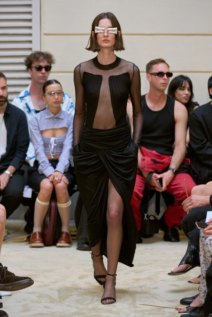 A fitted black silk sleeveless dress with a V-neckline and asymmetric draped design.