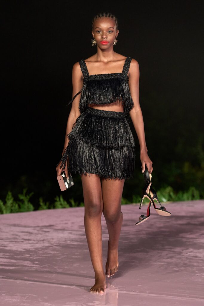 A fitted black silk dress featuring a sleeveless crop-top design with fringed and tiered detailing.