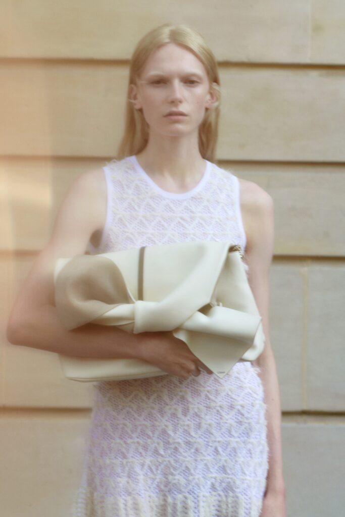 A fitted white lace dress with a sleeveless design and high-neck construction.