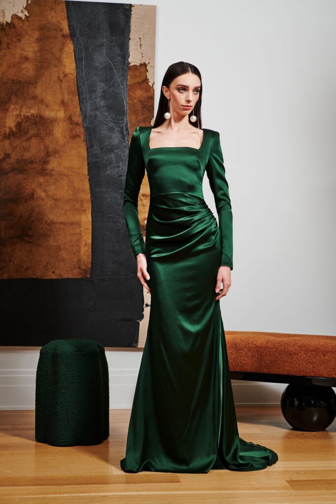 A fitted green silk gown with long sleeves and a square neckline, featuring a draped design.