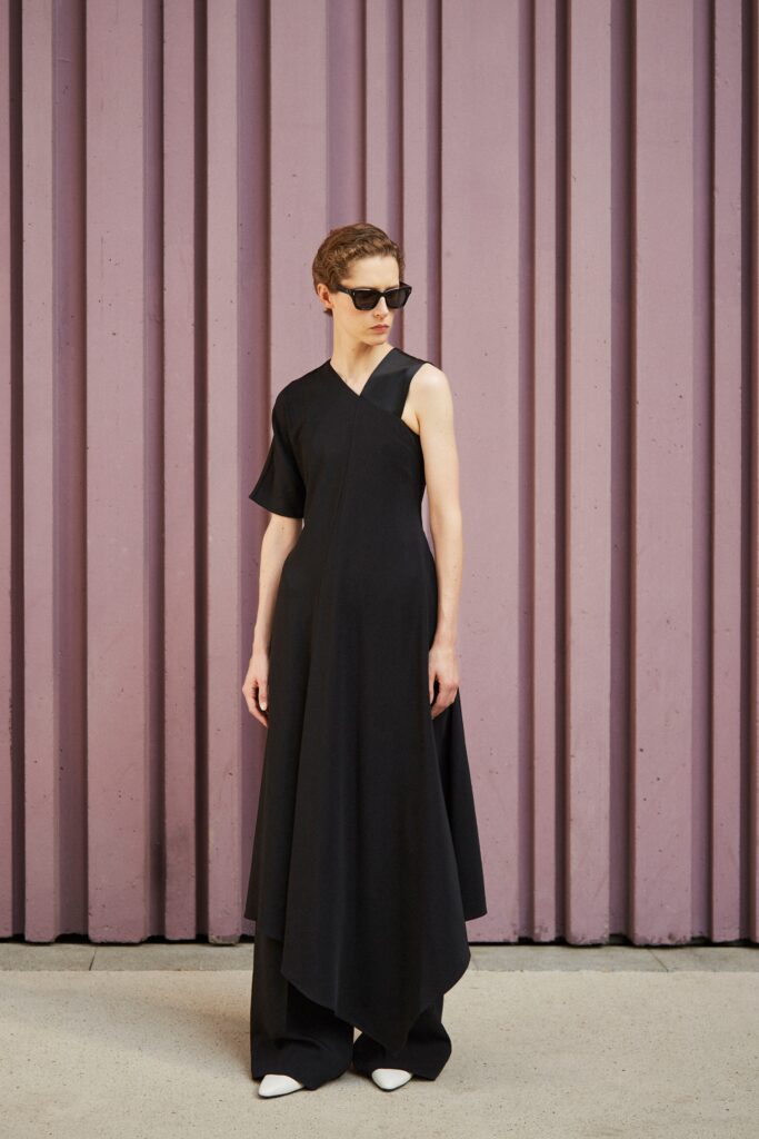 A fitted black sleeveless dress with an asymmetric design and V-neckline.