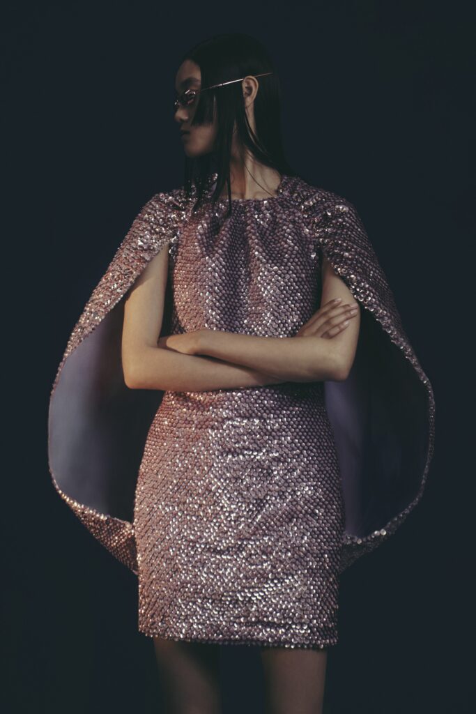 A fitted pink sequin mini dress with a sleeveless design and layered cape detail.