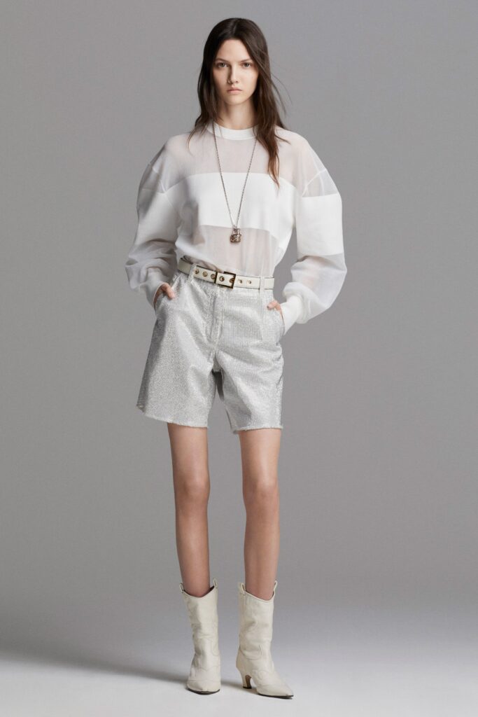 A relaxed white striped long-sleeve top paired with pleated silver shorts.