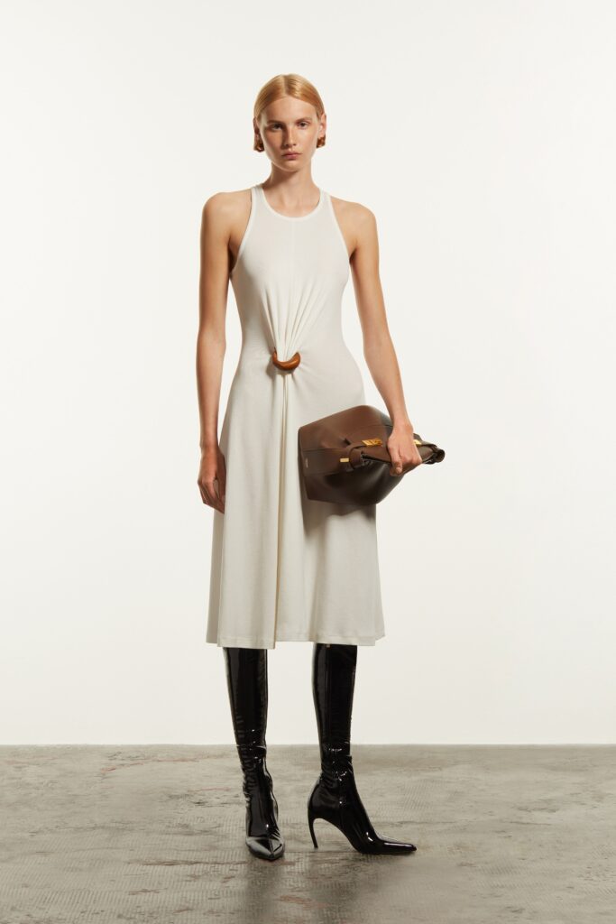 A fitted white sleeveless dress with a high neckline and asymmetric design detail.