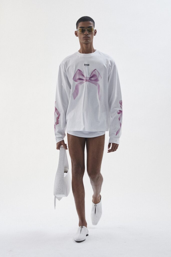 A relaxed white cotton shirt with long sleeves, featuring a pink bow print, paired with shorts.