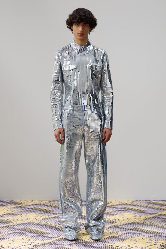 A fitted silver sequin jumpsuit with long sleeves and a collared neckline featuring a zippered detail.