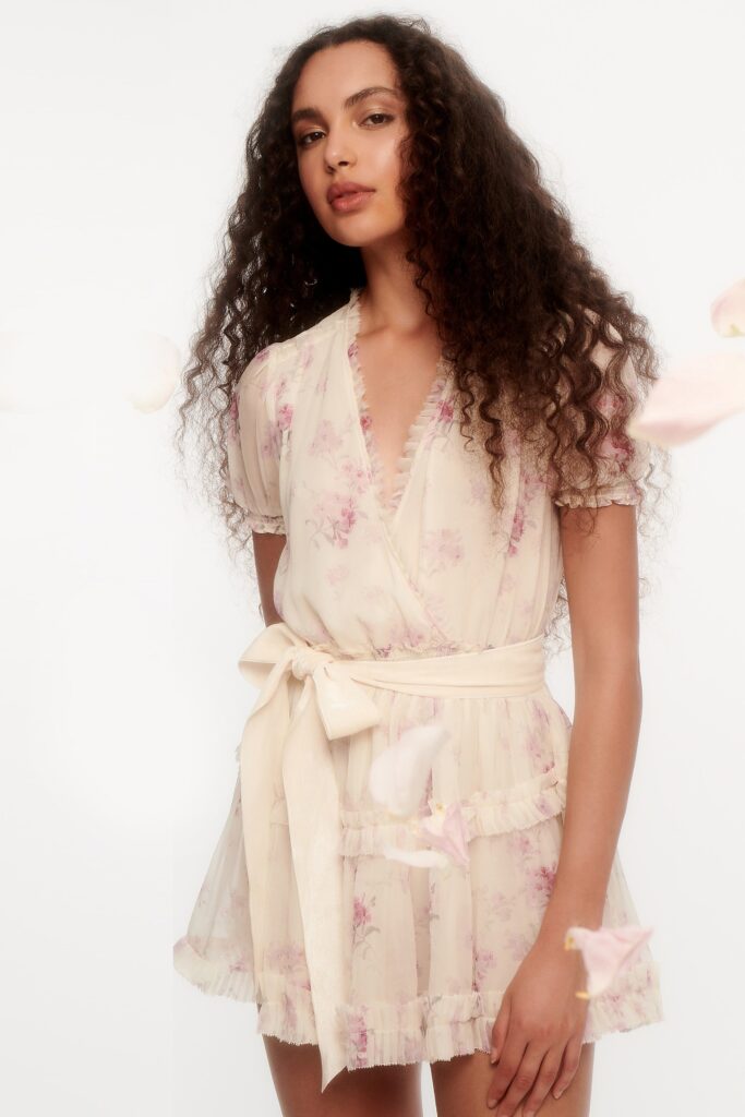 A fitted cream silk dress with short sleeves, a V-neckline, and flared ruffled details.