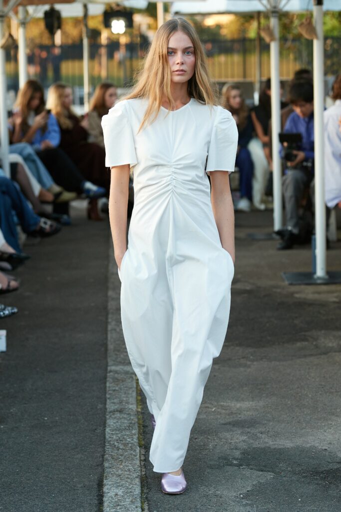 A relaxed white dress with short sleeves, a V-neckline, and pleated detailing.