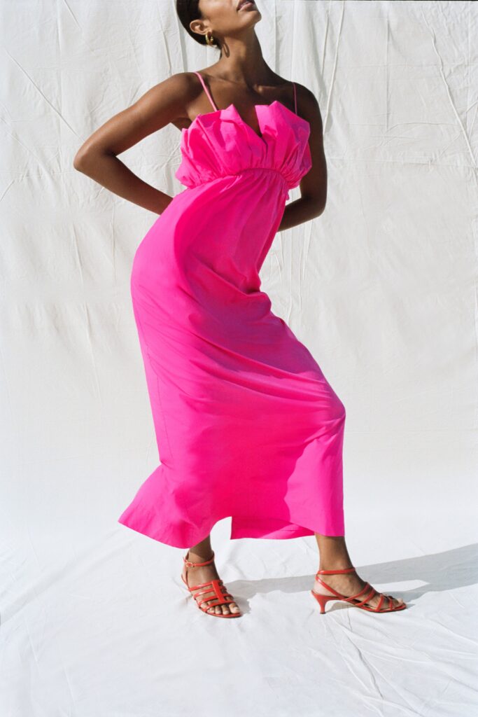 A fitted pink silk dress with a sleeveless design and V-neckline, featuring a maxi length.