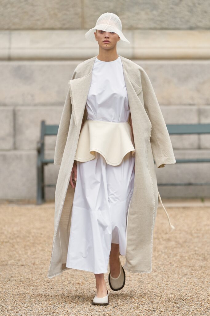 A relaxed white cotton dress layered under a beige coat with an asymmetric design.
