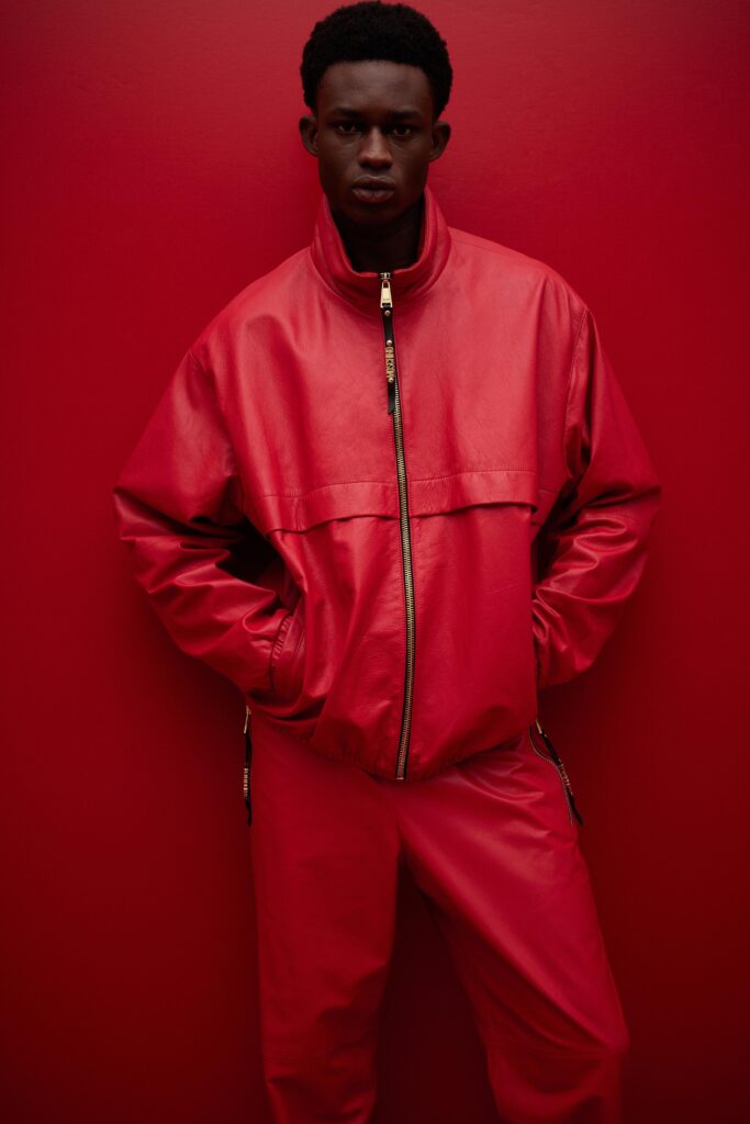 This ensemble features a relaxed-fit jacket crafted from vibrant red leather, complemented by matching pants. The jacket's zippered closure and collared design add a contemporary edge, while the overall silhouette exudes a bold, urban flair.