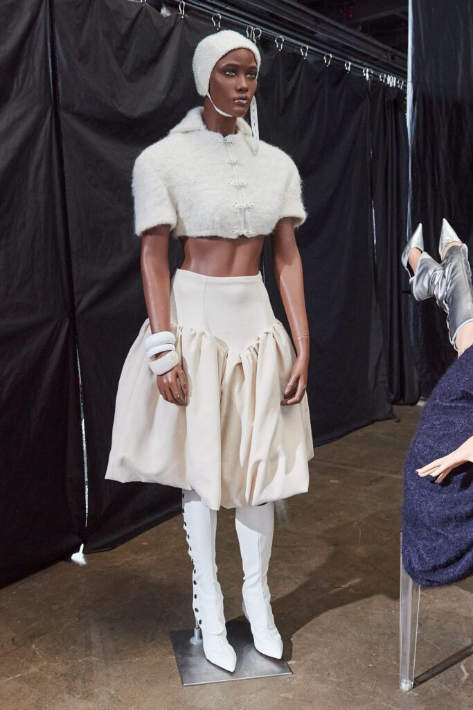A fitted white wool sleeveless top paired with a pleated beige skirt featuring an asymmetric design.