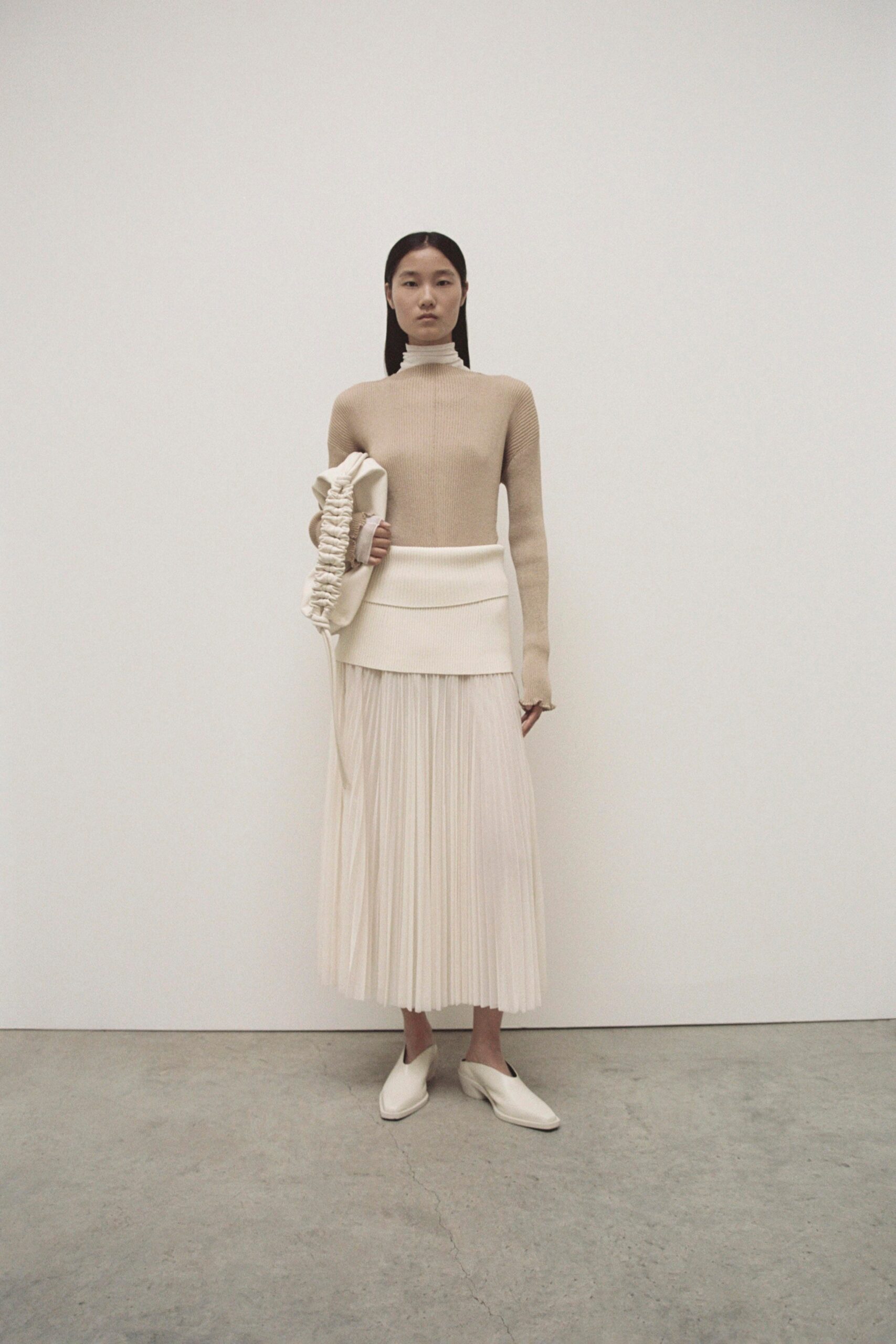A fitted beige wool sweater with long sleeves paired with a pleated white skirt.