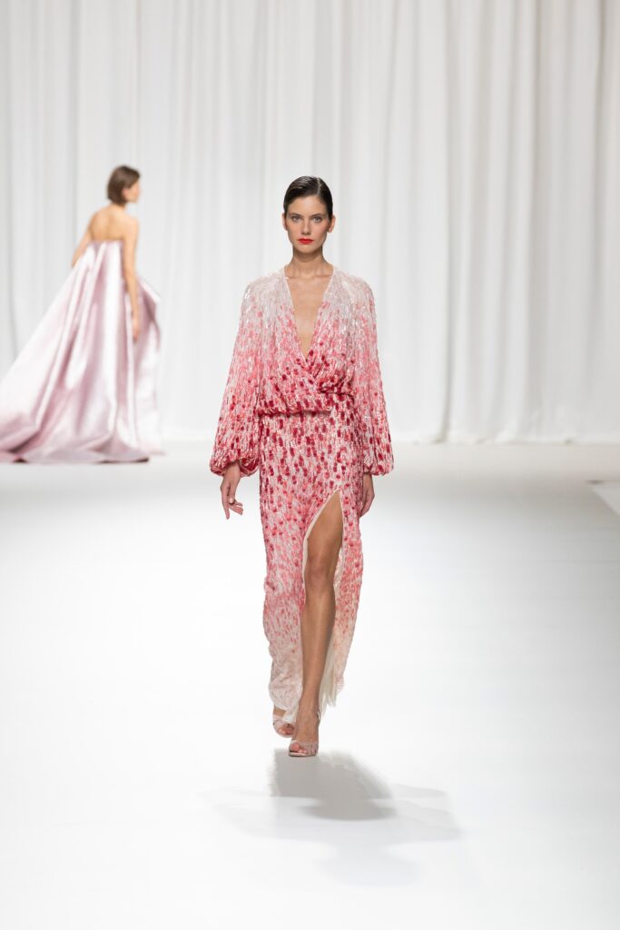 A fitted pink silk long-sleeve dress with a V-neckline and layered design featuring a slit.