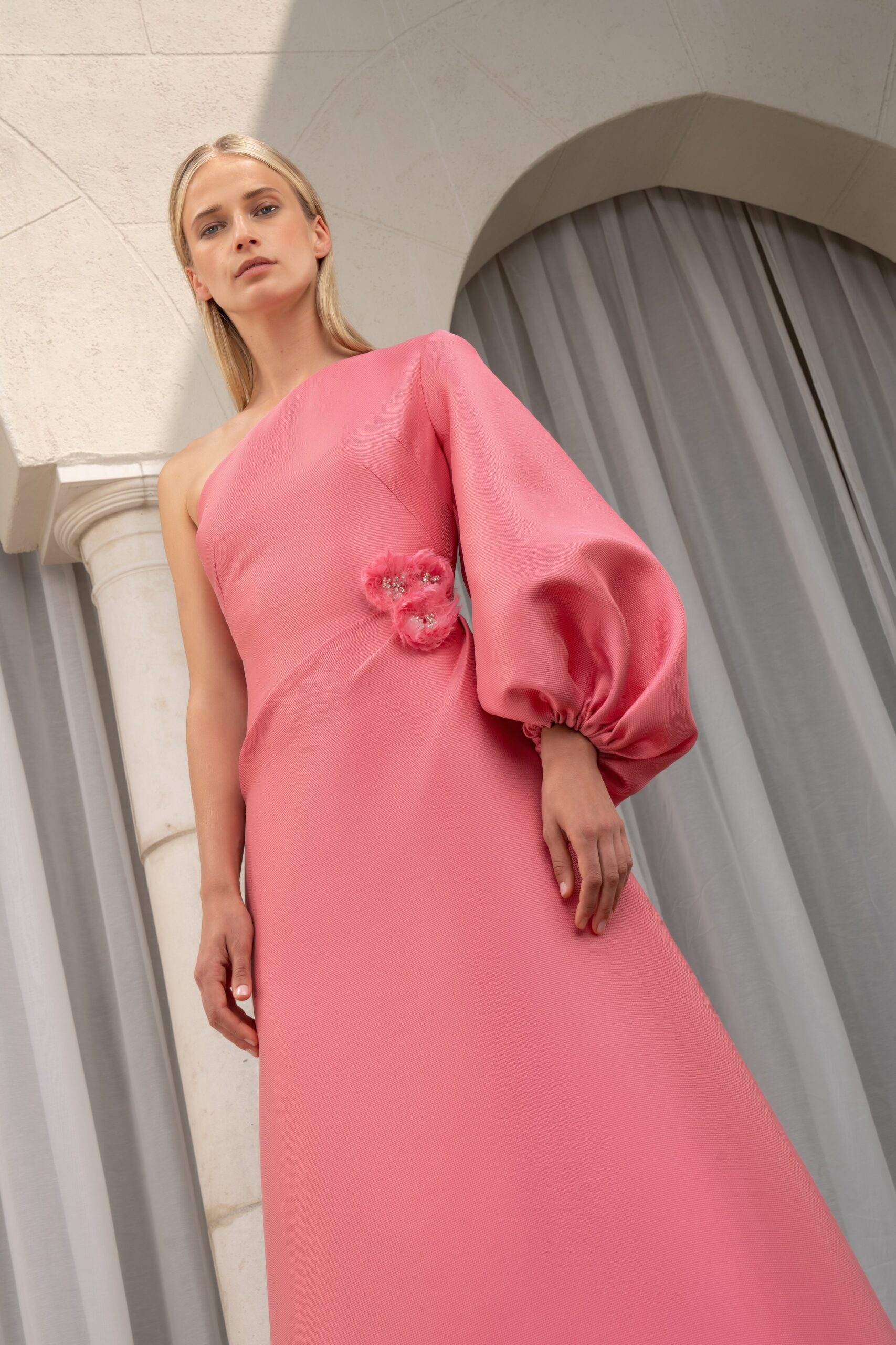 A fitted pink silk dress with an asymmetric design and a high neckline.