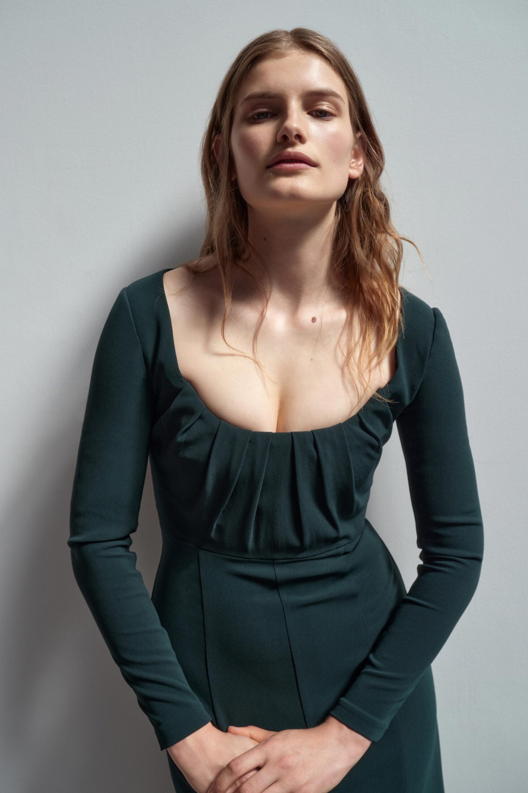 A fitted green dress with long sleeves and pleated detailing at the neckline.