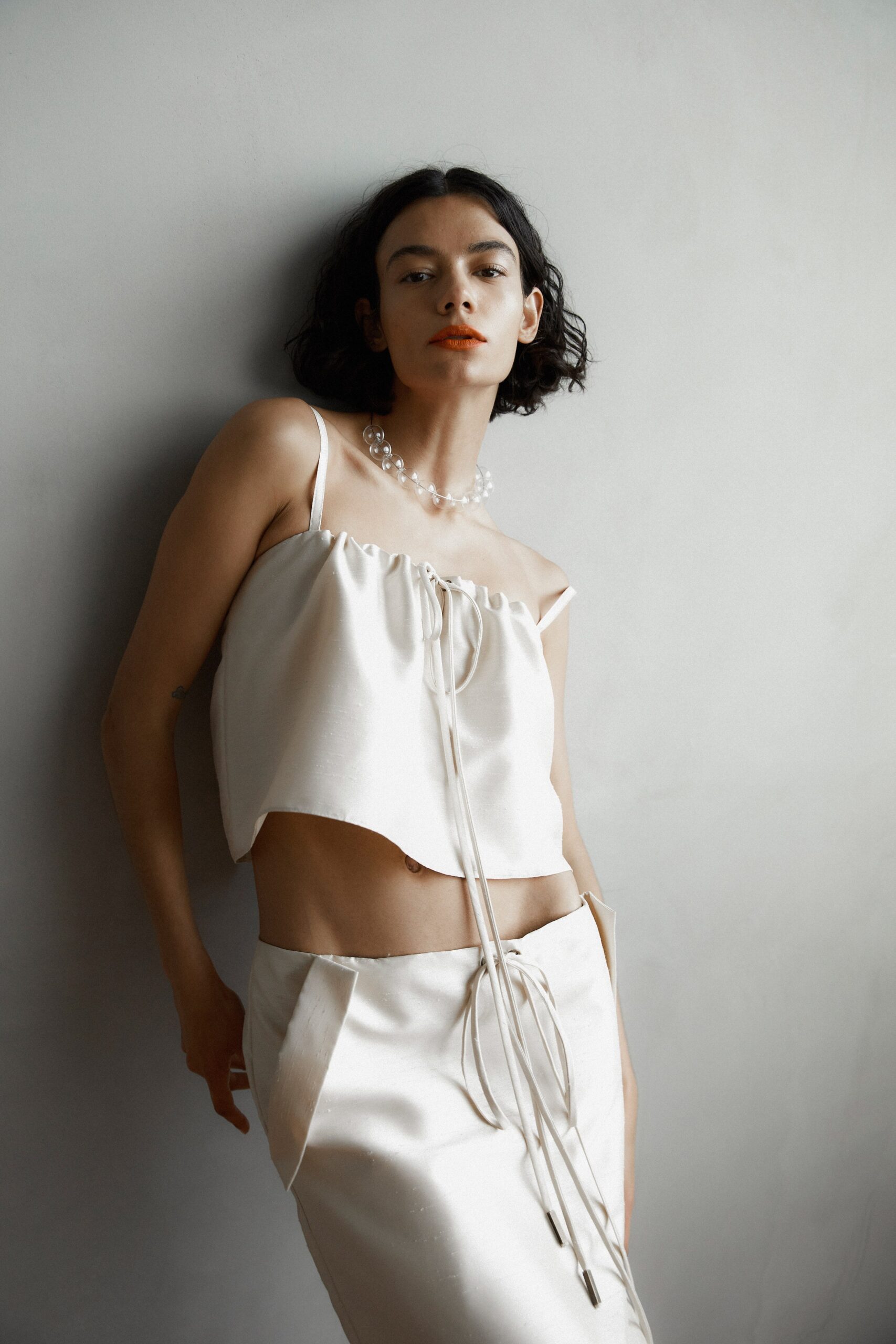 A fitted cream silk sleeveless top with a ruffled detail and an asymmetric skirt.