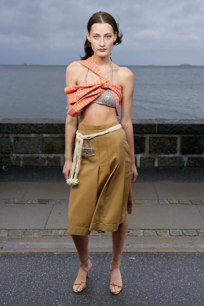 A fitted orange sleeveless top with an asymmetric design paired with a beige skirt.
