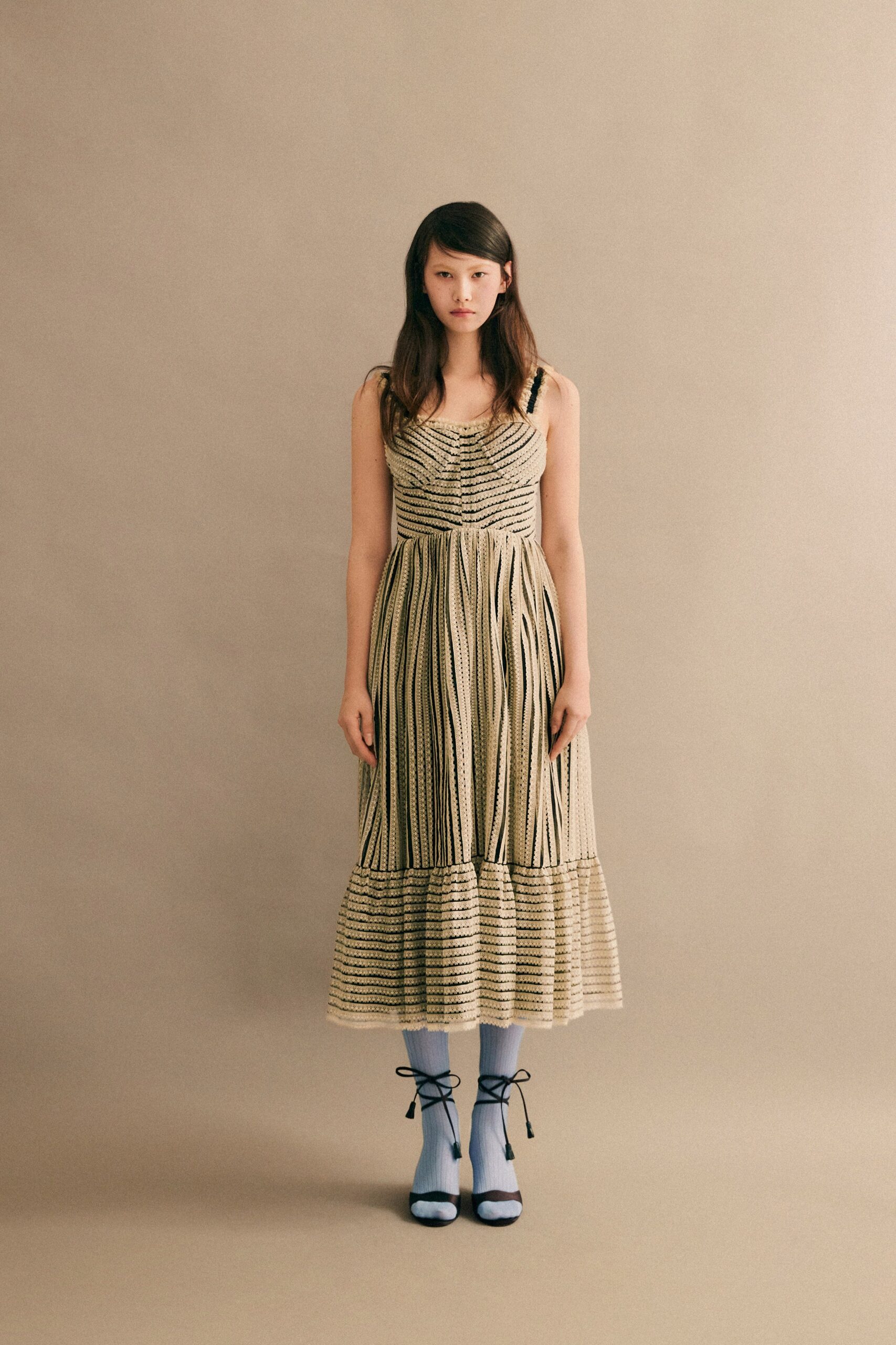 A fitted beige sleeveless dress with a V-neckline and tiered design.