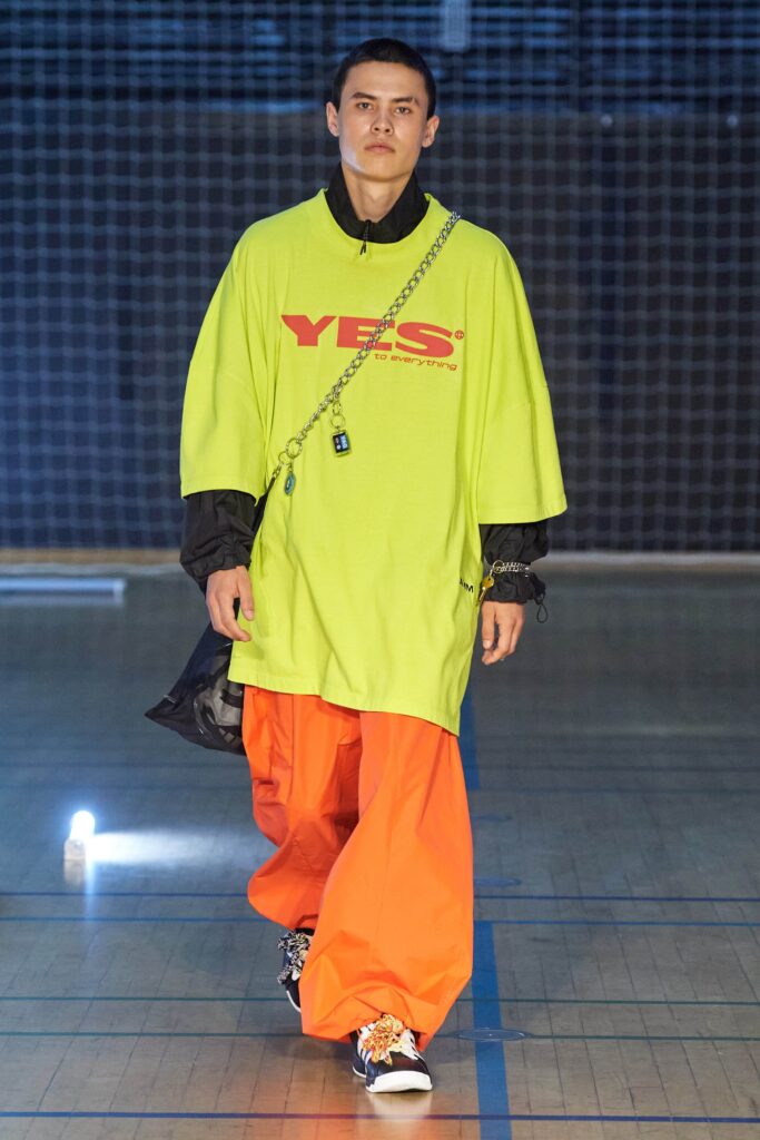 An oversized green shirt with a printed design paired with wide-leg orange pants.