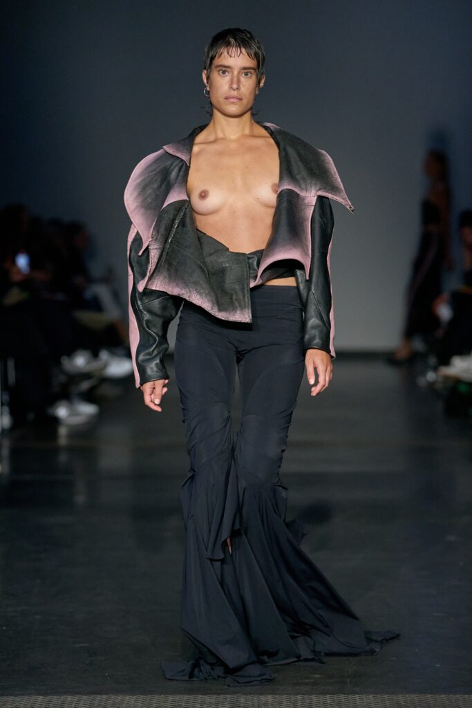 A fitted black leather jacket with pink accents paired with flared black pants.
